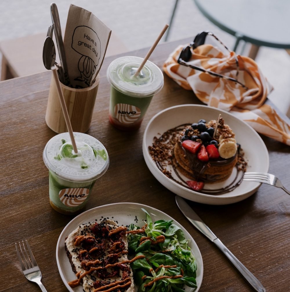 A brunch table at ARVO Bilbao with pancakes topped with berries, a plated savoury dish and iced drinks